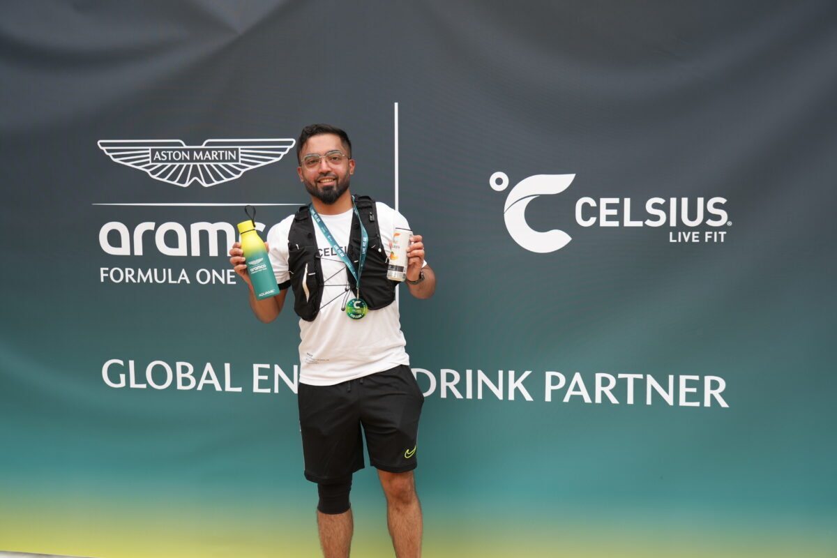 Man holding CELSIUS drinks in front of an Aston Martin Formula One and CELSIUS branded backdrop