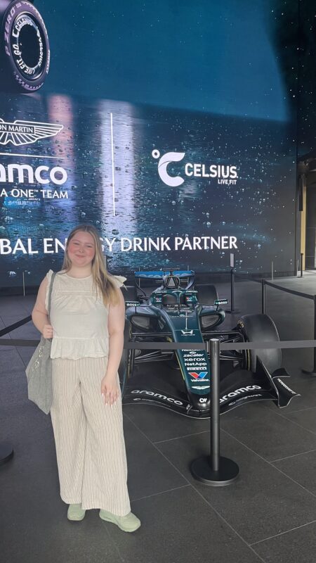 Woman posing beside an Aston Martin Aramco F1 car at a Celsius event display
